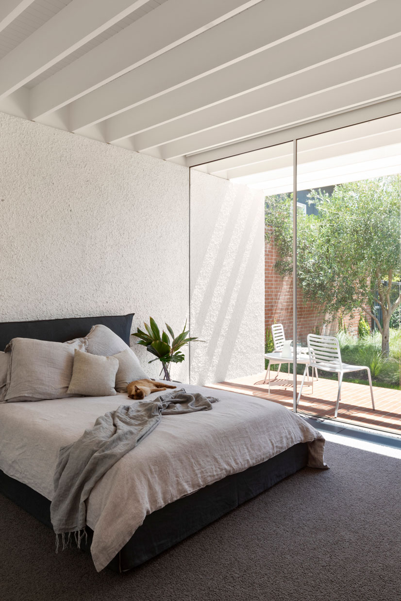 Melbourne Architects. The Master bedroom at Elwood House is a tactile combination of white stucco, white rhythmic rafters, and soft fabrics, connecting vividly to the green of the garden outside. 