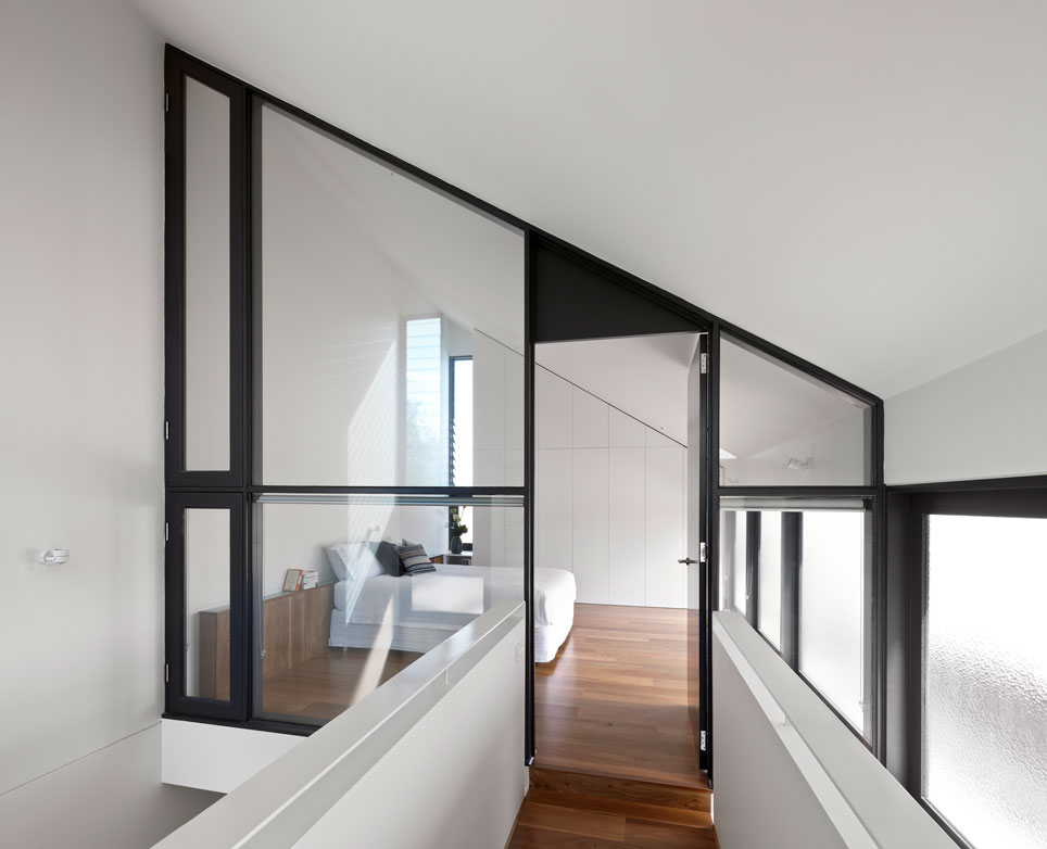 View to Master Bedroom. A bridge through the double storey void connects the master bedroom to the stairs and ensuite bathroom. A black glazed partition and windows separates the bedroom from the double-storey void, while allowing light and view to and from the master bedroom. Venetian blinds are used for privacy to the bedroom. 