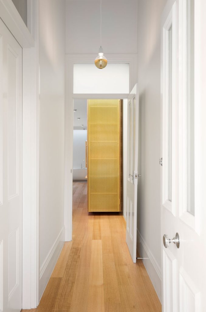 Melbourne Architects. Prahran House. View from Heritage section towards the new addition. A new gold coloured perforated metal joinery marks the separation between the old and new.